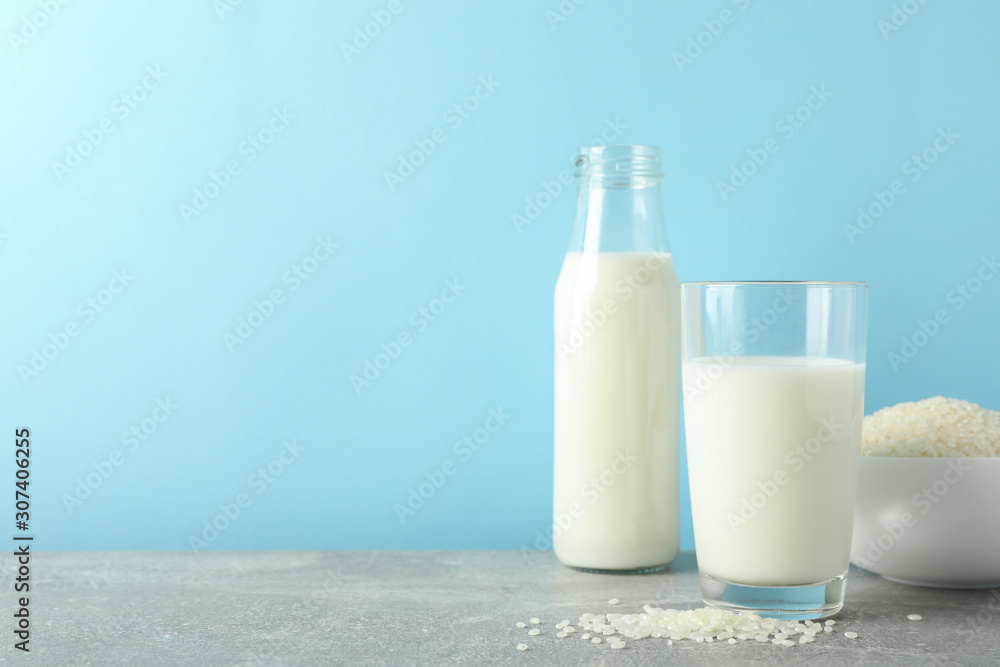 Bottle of rice milk, glass of rice milk, rice plate on grey table again blue background, space for text Bottle of rice milk, glass of rice milk, rice plate on grey table again blue background, space for text