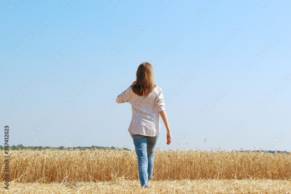 Teenage girl walking outdoors, back view. Happy girl walking in wheat field. People, nature, freedom concept. Teenage girl walking outdoors, back view. Happy girl walking in wheat field. People, nature, freedom concept.