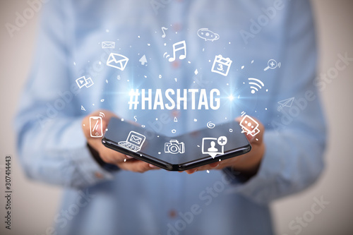 Businessman holding a foldable smartphone with #HASHTAG inscription, social media concept photo