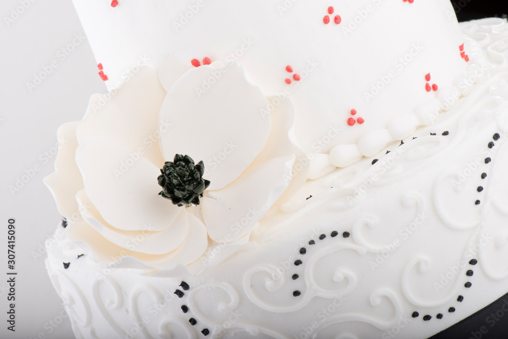 White wedding cake closeup with icing flower and black and red accents White wedding cake closeup with icing flower and black and red accents
