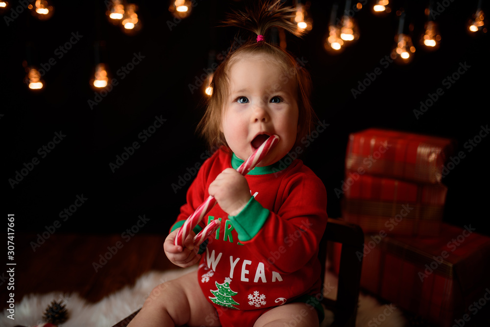 7 month old girl in a red Christmas costume on a background of retro garlands sits on a fur