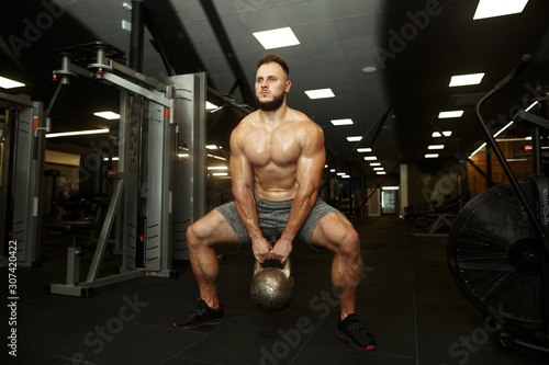 Strong handsome bearded man holding kettlebell and doing dumbbell front swings in the popular dark gym. SPORT IS LOVE.