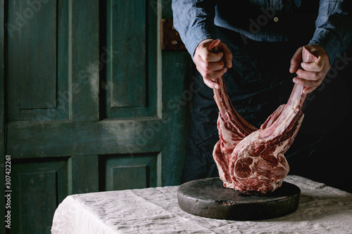 Quadro su tela Man's hands holding raw uncooked black angus beef tomahawk steaks on bones on linen table cloth