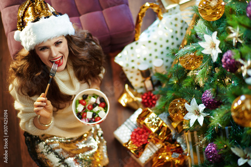 happy trendy housewife eating healthy salad near Christmas tree