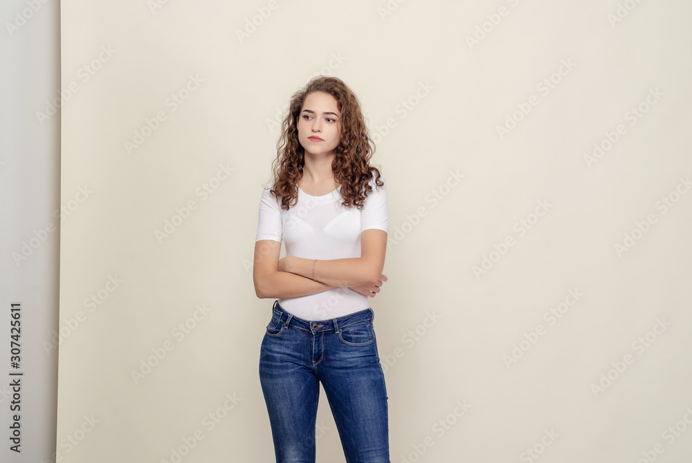 Portrait curly-haired girl in white T-shirt and jeans on light Portrait curly-haired girl in white T-shirt and jeans on light