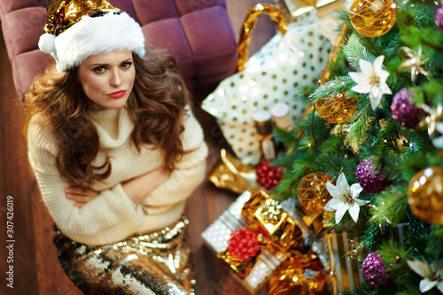 grumpy woman under decorated Christmas tree near present boxes