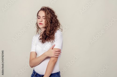 Beautiful sad girl stands on light yellow background, looks down.