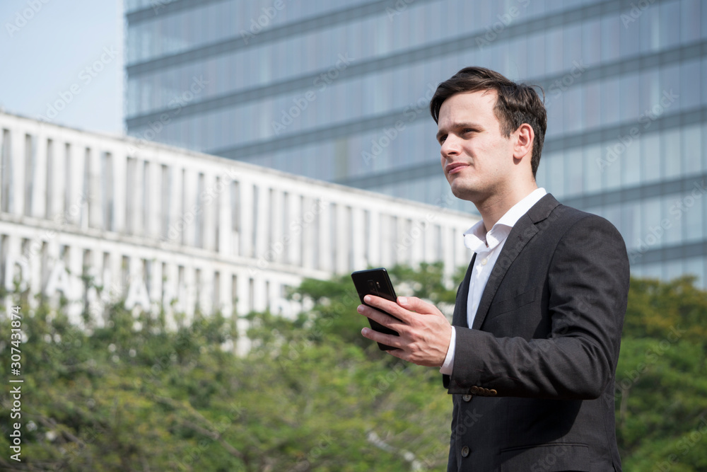 Adult man standing at road side while holding mobile phone. Adult man standing at road side while holding mobile phone.
