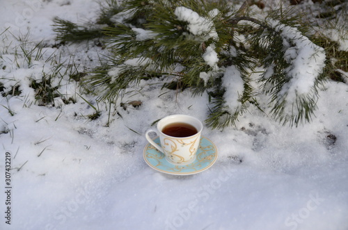 Winter. December. Against the backdrop of evergreens covered with white fluffy snow, there is a cup of freshly brewed fragrant black tea.