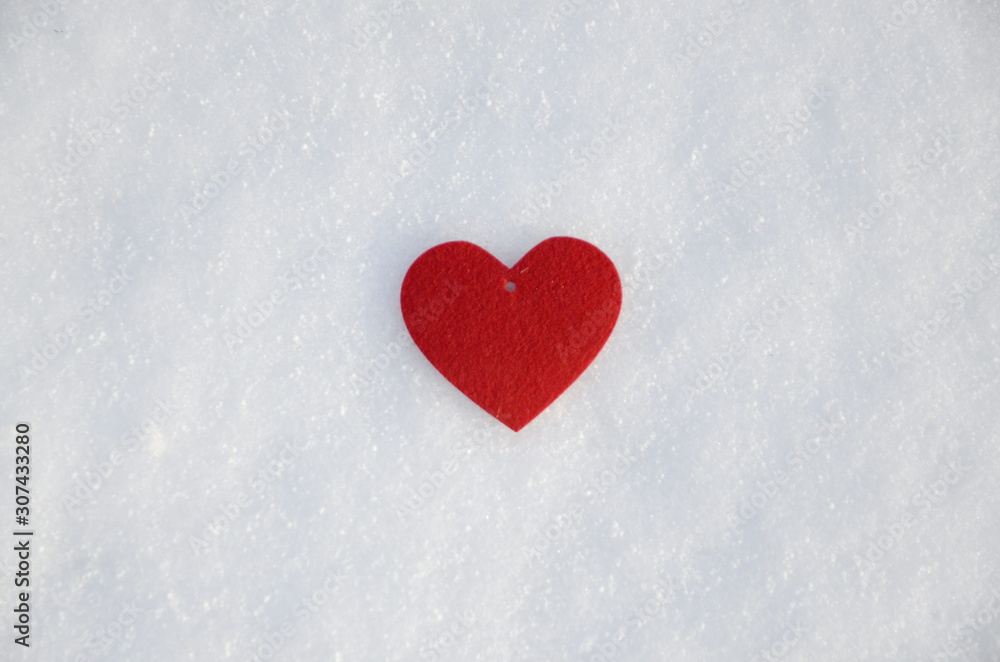 Winter. Holidays. Against the background of white fluffy snow lies a red felt heart.