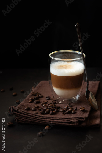 Front view on thermo glass cup of latte coffee on dark wooden table. Morning beverage