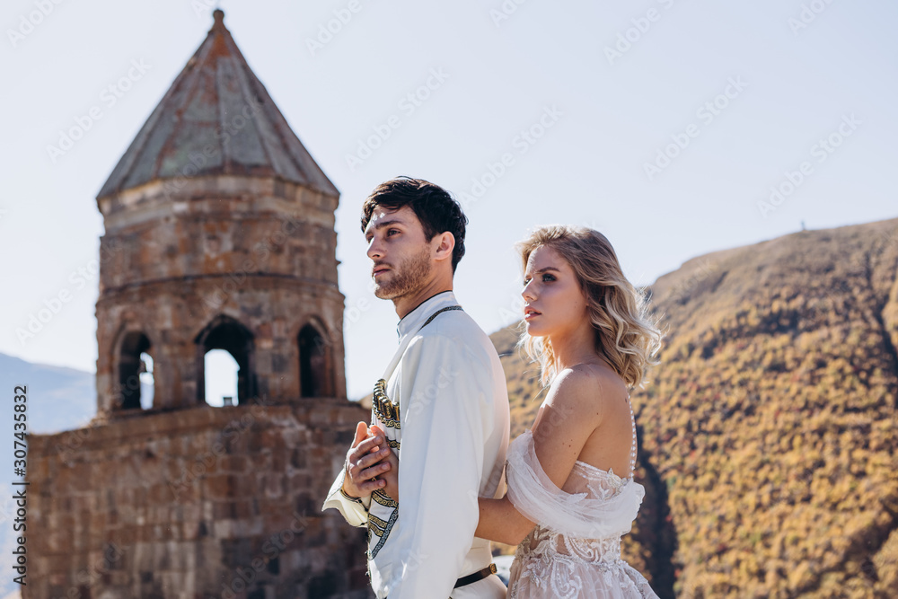 Georgian couple of brides are photographed against the backdrop of a wedding church at the top of a mountain