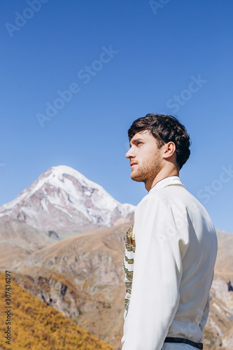 noise effect  selective focus  stylish Georgian man dressed in white national men s suit. Portrait of Georgian groom during wedding on Caucasus mountains