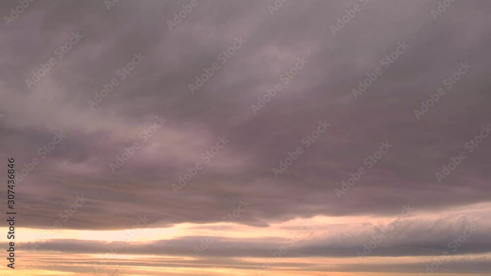 Time lapse of sky filled with thick clouds moving fast as sunset peeks through a break in the dense clouds in distant in 4K .mov Time lapse of sky filled with thick clouds moving fast as sunset peeks through a break in the dense clouds in distant in 4K .mov