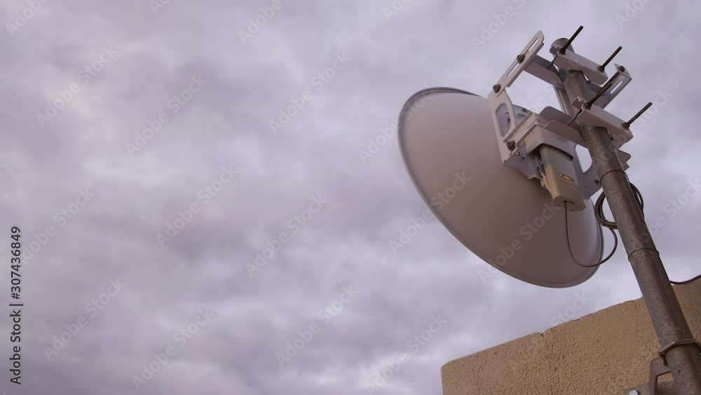 Time lapse of rain clouds moving fast across the sky on overcast day with a view of an internet antenna, dish, shuttle mounted against wall and lights blinking at the back showing signal in 4K Time lapse of rain clouds moving fast across the sky on overcast day with a view of an internet antenna, dish, shuttle mounted against wall and lights blinking at the back showing signal in 4K