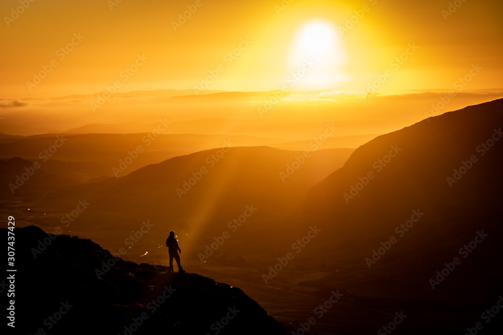 A hiker silhouetted against beautiful orange sunrise in mountains
