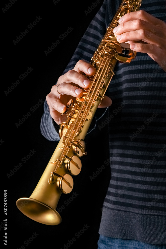Obraz premium soprano saxophone in the hands of a guy on a black background