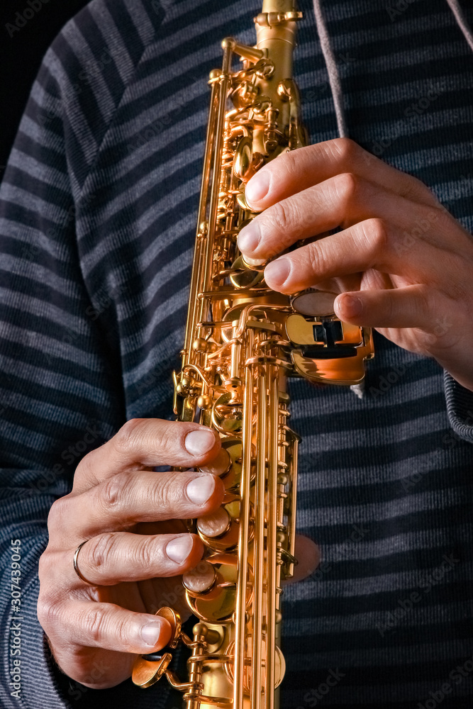 Naklejka premium soprano saxophone in the hands of a guy on a black background
