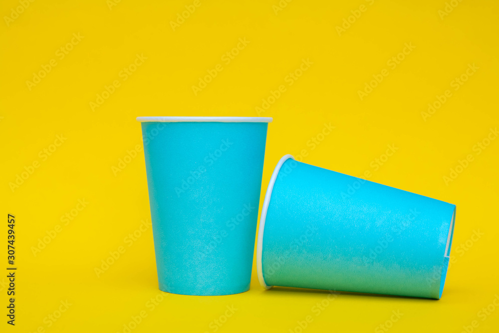 Two blue paper cups on yellow background. Copy, empty space for text Two blue paper cups on yellow background. Copy, empty space for text