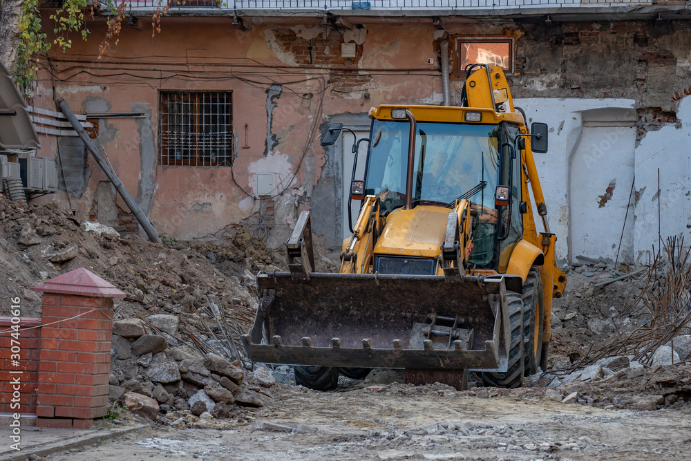 A large yellow excavator stands among the ruins of an old house