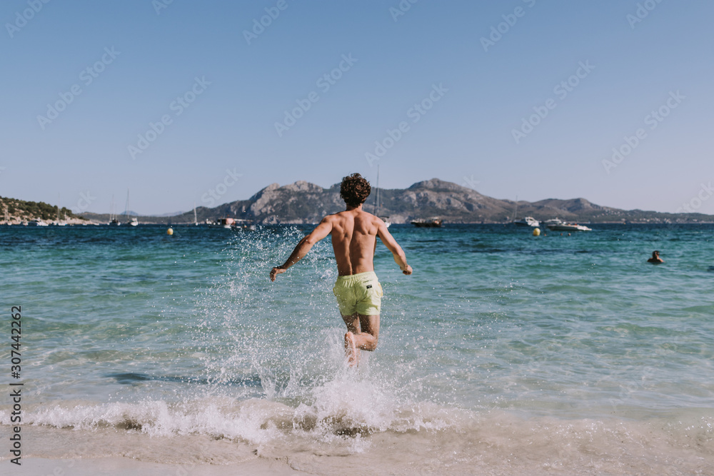 Man in swimsuit running in water on seashore Man in swimsuit running in water on seashore