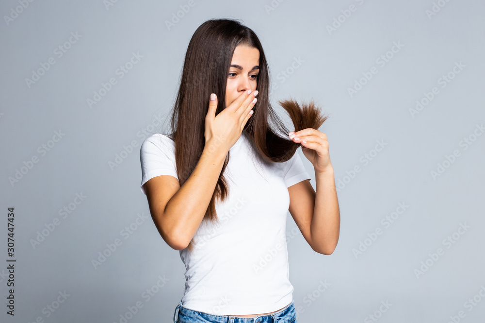 Sad girl looking at her damaged hair isolated on white background Sad girl looking at her damaged hair isolated on white background