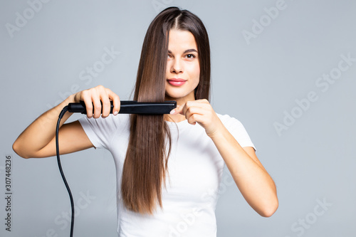 Smiling young woman straightening her hair with white background