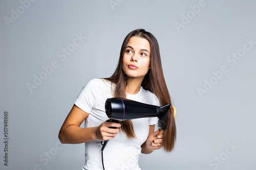Portrait of beautiful woman holding hair dryer isolated on gray background