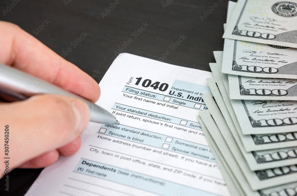 Obraz premium hand fills tax form 1040 on the background of dollars. Close-up. Business concept.