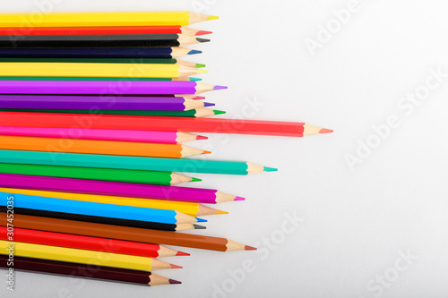 Group of mixed colourful pencils on a natural wooden background on the left side, isolated on white, children school or office suppliers photographed from top view with space for text