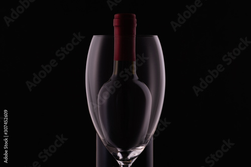 Red wine glass and a wine bottle with reflections on black background