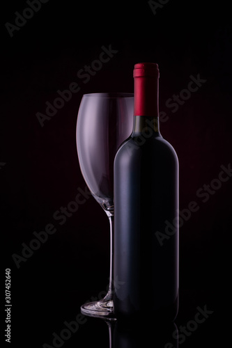 Red wine glass and a wine bottle with reflections on black background