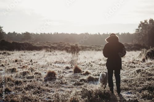 Man walking dog on frosty heathland in golden light