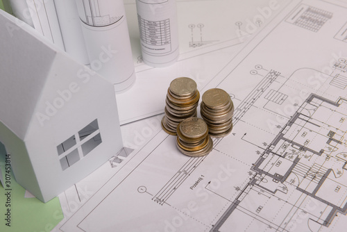 White family paper house , stack of money coins, house projects plan and blueprints on mint background paper. Minimalistic and simple concept, style. Vertical orientation.