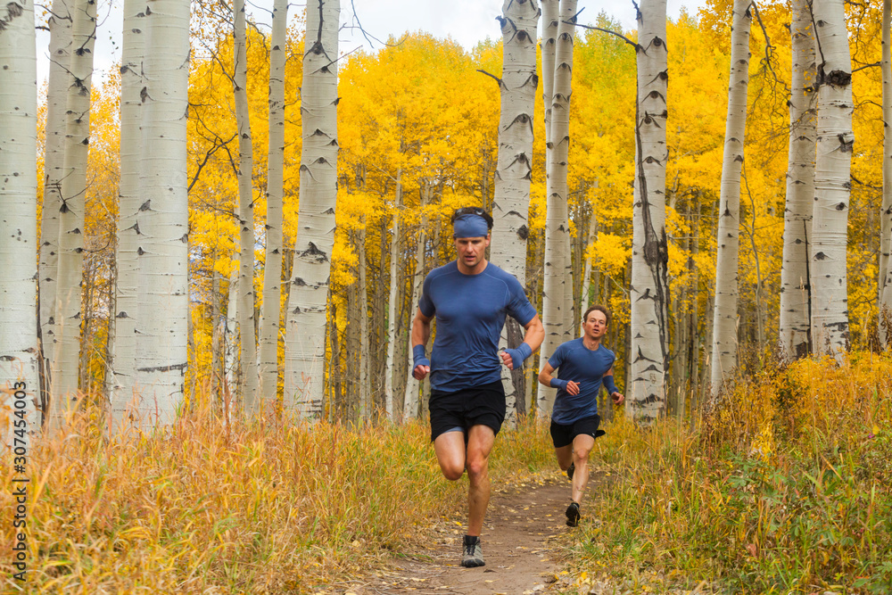 Men trail run through aspen forest with fall color in Vail, Colorado Men trail run through aspen forest with fall color in Vail, Colorado