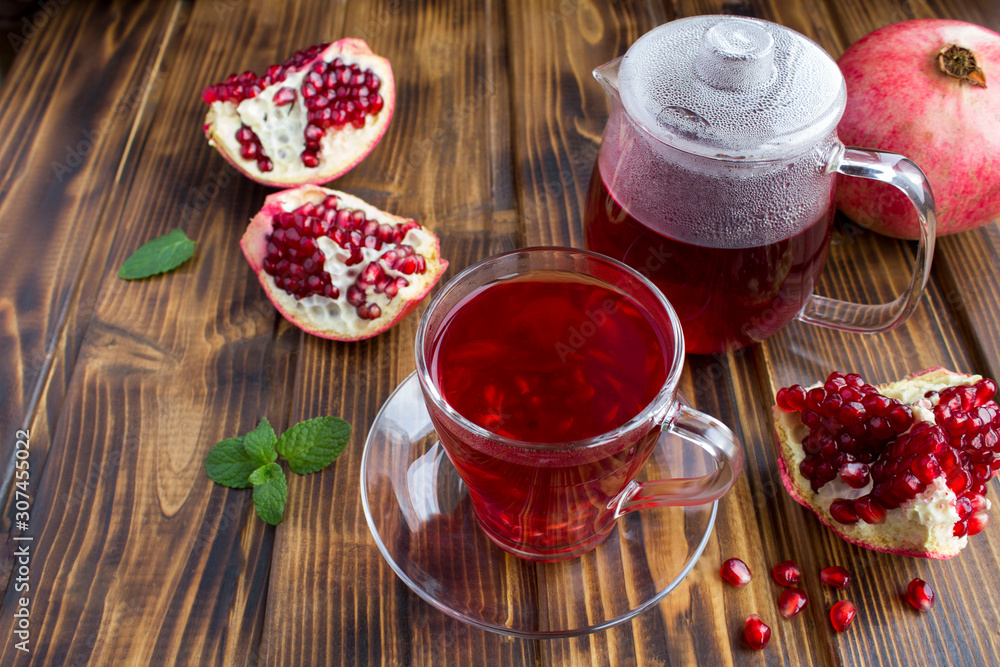 Pomegranate tea in the glass cup and teapot on the brown wooden background Pomegranate tea in the glass cup and teapot on the brown wooden background