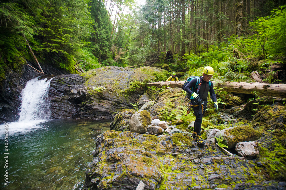 hiker walks over rocky terrain beside waterfall in dense forest. hiker walks over rocky terrain beside waterfall in dense forest.