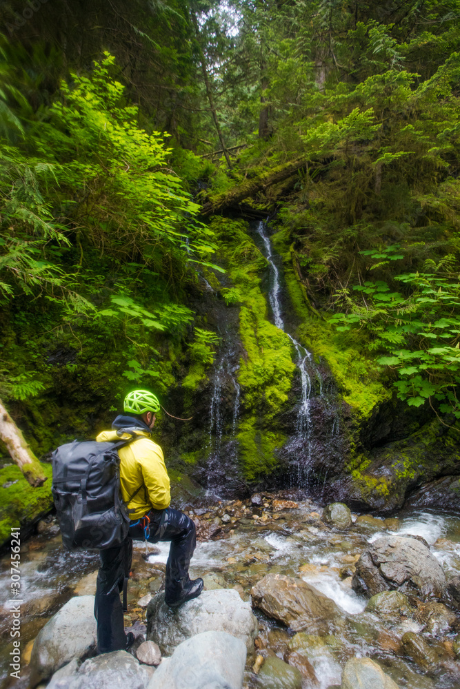 wet hiker wearing backpack looks at small waterfall. wet hiker wearing backpack looks at small waterfall.