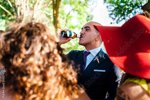 Thirsty groom drinking beer surrounded by guests after wedding celeb photo