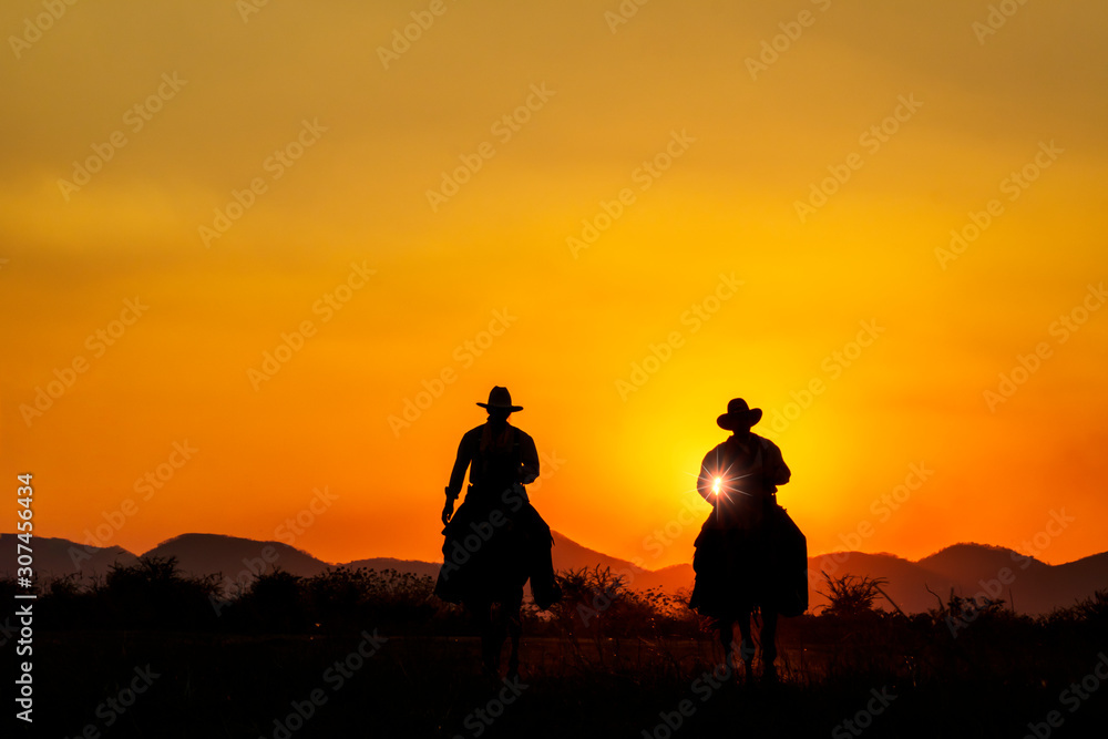 Silhouette image of two cowboys riding horseback at sunset with mountain range background