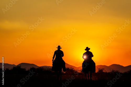 Silhouette image of two cowboys riding horseback at sunset with mountain range background