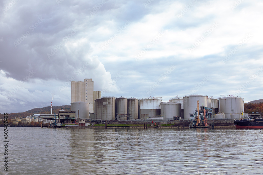 View on Rhine river with Industrial Tanks for liquid fuels storage. Industrial buildings on the bank of the river. Waterway fuel transport Switzerland. View on Rhine river with Industrial Tanks for liquid fuels storage. Industrial buildings on the bank of the river. Waterway fuel transport Switzerland.
