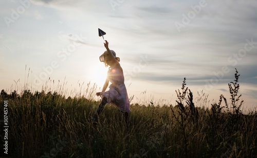 girl chasing a paper aeroplane in a meadow at sunset