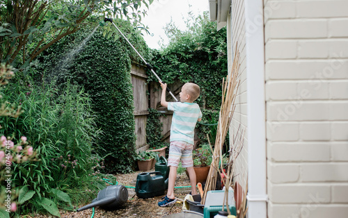 young boy watering his english country garden in summer photo