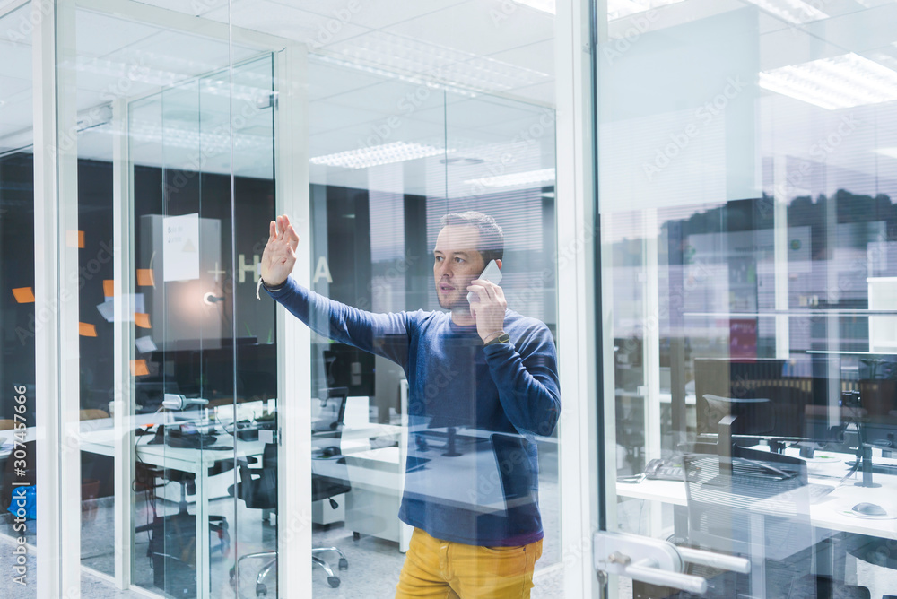 Side view of businessman talking on smart phone while standing against office wall Side view of businessman talking on smart phone while standing against office wall