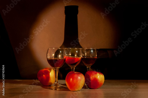 Three glasses with calvados and apples on the table on the background of the bottle