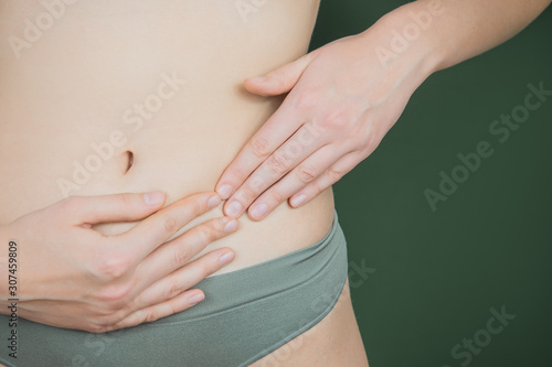 Woman holding hands near panties in the area of reproductive organs on green background.  Gynecological concept. Problems with menstrual cycle and gynecological diseases photo
