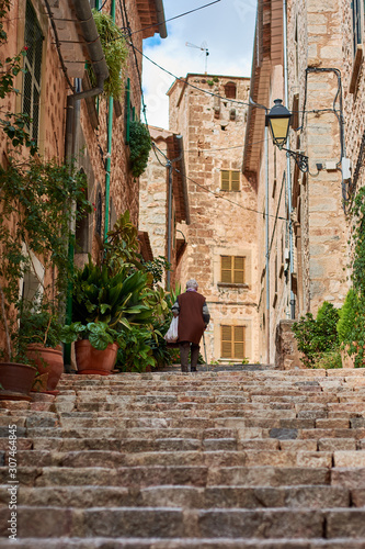 Elderly woman climbing stone stairs in Mallorcan village. Street with ornamental plants. Fornalutx  Mallorca
