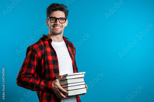 Wallpaper Mural European student in red plaid shirt on blue background in studio holds stack of university books from library