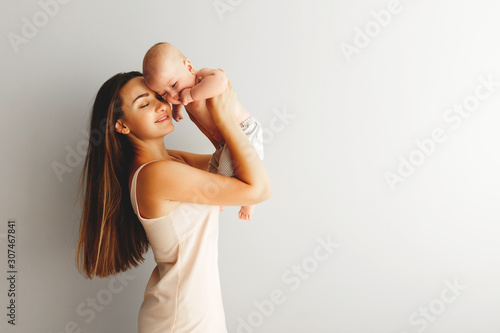 beautiful happy mother holds her baby on a plain light background.